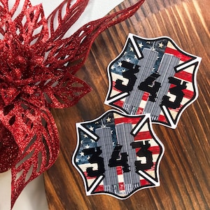 May include: Two star-shaped stickers with a patriotic design featuring the American flag, the Twin Towers, and the number 343 in black. A red glittery floral decoration is in the background.
