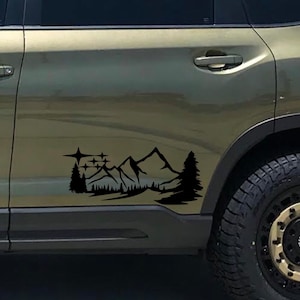 May include: A black vinyl decal of a mountain range with stars and trees, applied to the side of a green SUV.