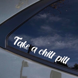 May include: A white vinyl sticker on a car window that says "Take a chill pill" in a cursive font.