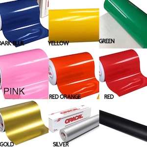 Puede incluir: Una colecci&oacute;n de rollos de vinilo en varios colores: azul oscuro, amarillo, verde, rosa, rojo-naranja, rojo, dorado, plateado y negro. Cada color est&aacute; etiquetado. La marca "ORACAL" es visible en una caja.