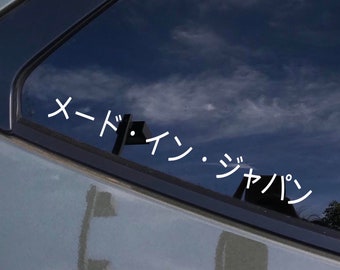 Può includere: Un adesivo in vinile bianco sul finestrino di un'auto con il testo giapponese "メードイン・ジャパン" che si traduce in "Made in Japan".