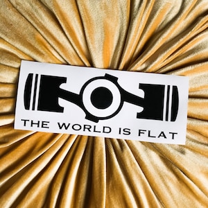 May include: A white sticker with a black silhouette of a piston and connecting rod. The text "THE WORLD IS FLAT" is printed below the image.