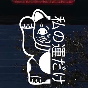 May include: White vinyl decal of a Japanese Maneki-Neko, or lucky cat, with its paw raised. The cat is holding a coin and has a large, round head. The text "招き猫" is written vertically on the right side of the cat, which translates to "beckoning cat".