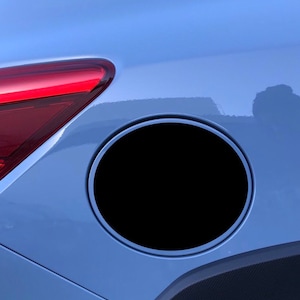 May include: A blue car with a black fuel cap door. The fuel cap door is round and has a silver trim.