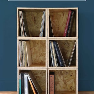 May include: A set of six wooden crates stacked on top of each other to create a shelf unit. The crates are made of plywood and have a natural wood finish. The shelves are filled with books and vinyl records.
