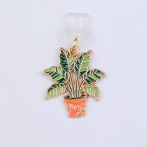 May include: A gold-toned metal enamel charm shaped like a potted plant with green and light green leaves in an orange pot. The charm is attached to a white display card featuring the text Duchess Gems STUDIO printed in black ink.