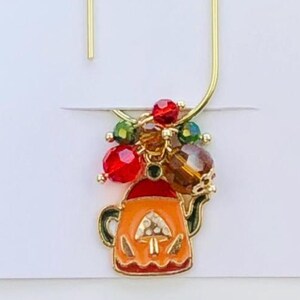 May include: A gold-colored bookmark with a decorative charm. The charm features a small orange teapot with a pumpkin design, accented with red, green, and amber-colored beads. The text "Duchess Gems" is printed on the white card.