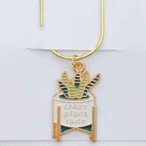 May include: A gold-colored bookmark with a charm featuring a white planter with a green and yellow succulent and the text "crazy plant lady." The bookmark has the text "Duchess Gems" at the top.