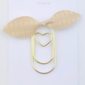 May include: Gold double-loop paper clip with a heart-shaped cutout, decorated with a beige bow with a checkered pattern. Duchess Gems Studio.