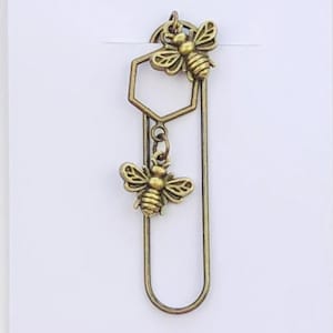 May include: A bronze metal bookmark with two bee charms and a honeycomb-shaped detail. The bookmark is displayed on a white card with the text "Duchess Gems STUDIO".