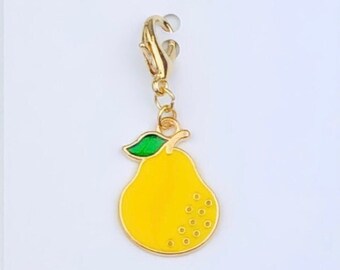 May include: A gold-colored charm with a yellow pear design. The pear has a green leaf and a gold outline. The charm has a lobster claw clasp.