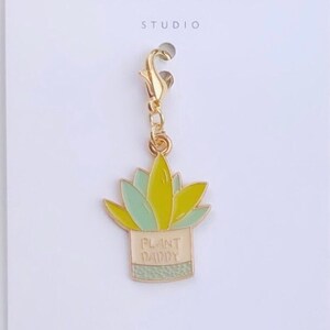 May include: Gold charm with a green and yellow plant in a pot that says "Plant Daddy".