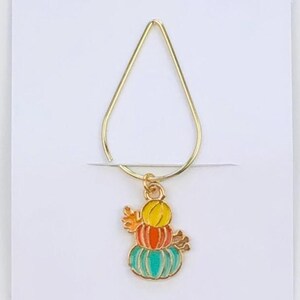May include: A gold-coloured metal bookmark with a colourful pumpkin charm. The charm features three stacked pumpkins in yellow, orange, and teal. The bookmark is attached to a white card with the text "Duchess Gems STUDIO".