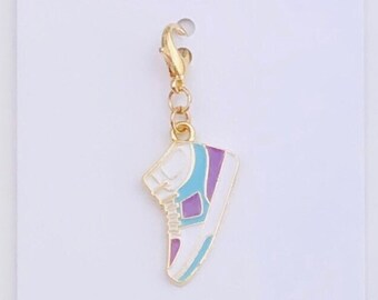 May include: Gold charm with a white sneaker with purple and blue accents. The charm has a gold lobster clasp. Duchess Gems Studio is printed on the white card behind the charm.