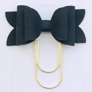 May include: Black bow with scalloped edges attached to a gold double-loop paper clip. The bow and clip are on a white card with the text "Duchess Gems Studio".