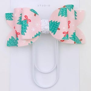 May include: A pink Christmas tree patterned bow with a white center, attached to a white paper clip. The bow features green Christmas trees, red bows, and white stars. The text "Duchess Gems STUDIO" is printed on the white card.
