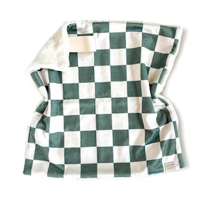May include: A soft, plush blanket with a green and white checkerboard pattern. The blanket has a white, fuzzy backing and a small tag with the text "cotton & zoo".