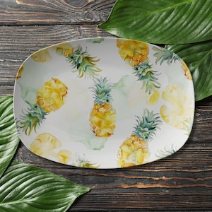 May include: White oval serving platter with a pineapple pattern. The platter has a white background with yellow and green pineapples.