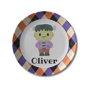 May include: A purple, orange, and black checkered plate with a cartoon monster wearing a purple shirt and brown pants. The plate says "Oliver" in black text.