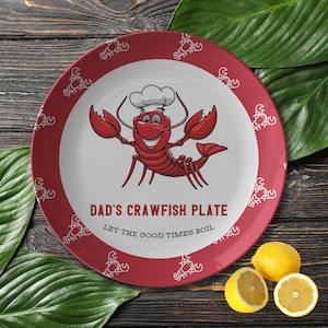 May include: Red ceramic plate with a white border and a cartoon crawfish wearing a chef's hat. The plate has the text "Dad's Crawfish Plate" and "Let the good times boil".