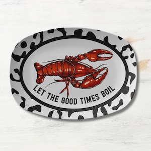 May include: A white oval serving platter with a black and white animal print border. The center of the platter features a red lobster with the text "Let the good times boil" in black.