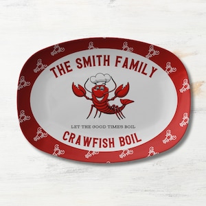 May include: Red oval serving platter with a white border and a cartoon crawfish wearing a chef's hat. The platter has a white background with the text "THE SMITH FAMILY LET THE GOOD TIMES BOIL CRAWFISH BOIL". The border is decorated with a repeating pattern of white crawfish.