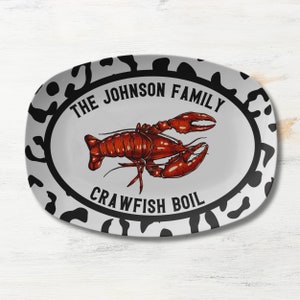 May include: White oval serving platter with a black and white splatter design. The platter has a black circle in the center with the text "The Johnson Family Crawfish Boil". A red crawfish is pictured inside the circle.