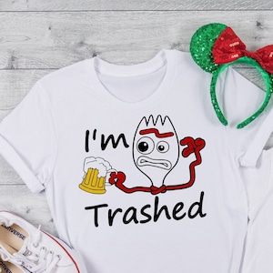 Puede incluir: Dos camisetas blancas con una imagen de dibujos animados de un tenedor sosteniendo una jarra de cerveza y el texto "I'm Trashed". La camiseta más grande tiene una diadema roja con lazo en la parte superior. La camiseta más pequeña tiene una piruleta colorida a su lado.