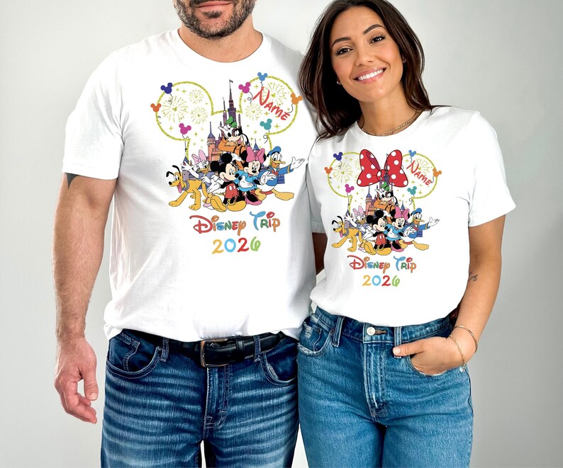 May include: White t-shirts featuring a colorful Disney character design. The design includes Mickey Mouse, Minnie Mouse, and other characters, with the text "Disney Trip 2026". The shirts have a round neckline and short sleeves.