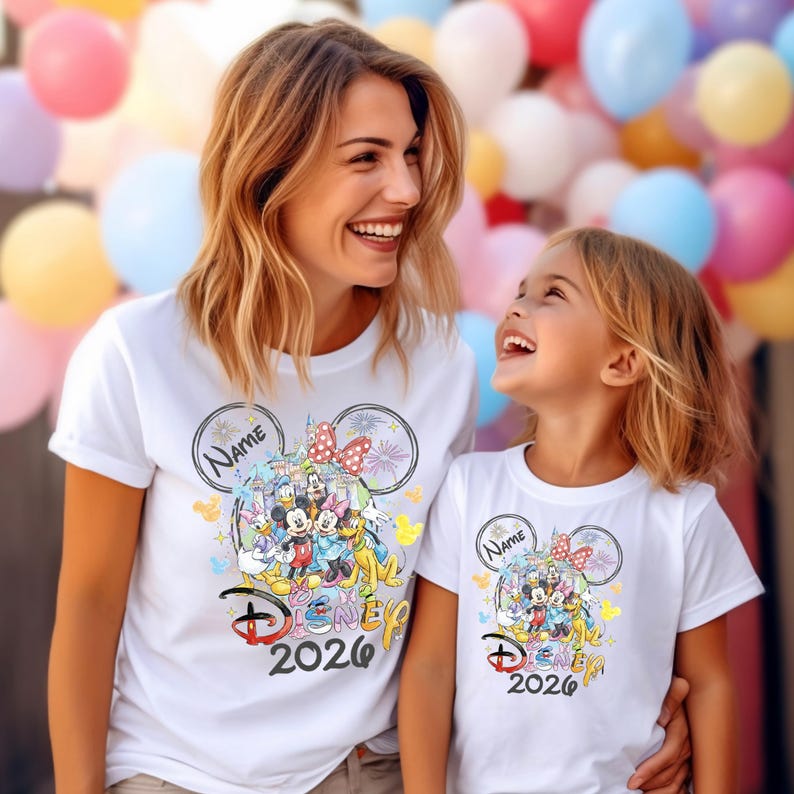 May include: White t-shirts featuring a Disney design with Mickey Mouse, Minnie Mouse, and other characters. The shirts have the text "Disney 2026" and a space for a name. The design includes fireworks and colorful accents.