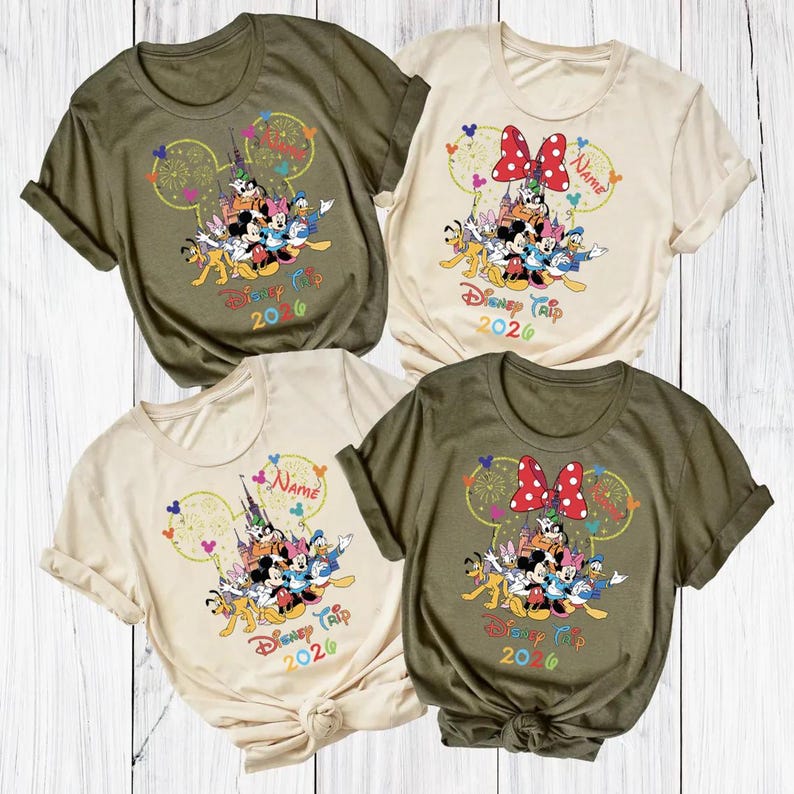 May include: Four t-shirts in olive green and cream colors, each featuring a colorful graphic of Disney characters. The design includes Mickey Mouse ears, fireworks, and the text "Disney Trip 2020". Some shirts have a red bow.
