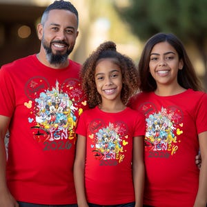 May include: Three people wearing matching red t-shirts with a Disney theme. The shirts feature a colorful graphic of Disney characters, a castle, fireworks, and the text "DISNEY 2020".