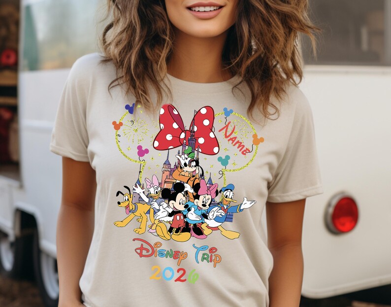 May include: Beige t-shirt featuring a colorful graphic of Disney characters, including Mickey and Minnie Mouse, Donald Duck, and Goofy. The design includes a red polka-dot bow, a castle, and the text "Disney Trip 2024" with a space for a name.