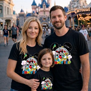 May include: A family of three wearing matching black t-shirts with a colorful Disney character design. The shirts have the text "2020 Disney Trip" and feature Mickey Mouse, Minnie Mouse, and other characters. The family is posing in front of a castle.