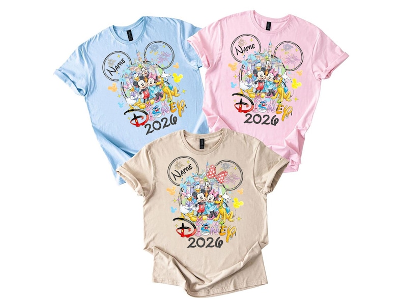 May include: Three short-sleeved t-shirts in light blue, pink, and beige. Each shirt features a colorful graphic of Disney characters, the text "Disney 2026", and space for a name within a Mickey Mouse ear design.