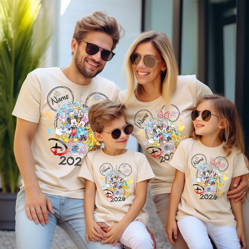 May include: Beige t-shirts with a colorful Disney graphic featuring Mickey and Minnie Mouse, a castle, and the text "Disney 2020". Each shirt has a circular design with the word "Name" above the graphic.