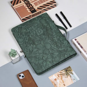 May include: A green leather journal with a floral embossed design. The journal has a zipper closure and a metal ring for attaching a pen.
