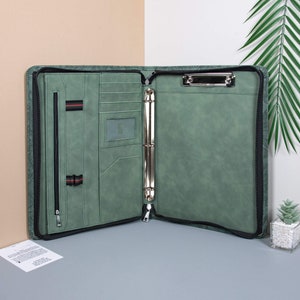 May include: A green leather zippered binder with a metal ring mechanism and a built-in clipboard. The binder has multiple pockets and a zippered compartment.