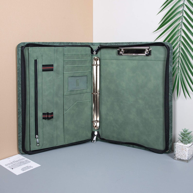 May include: A green leather zippered binder with a metal ring mechanism and a built-in clipboard. The binder has multiple pockets and a zippered compartment.