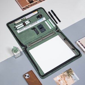 May include: A green leather binder with a zipper closure, a ring binder mechanism, and a built-in notepad. The binder has multiple pockets and slots for pens, cards, and other accessories. The text "Heading Bitsa Dips" is printed on the front of the binder.