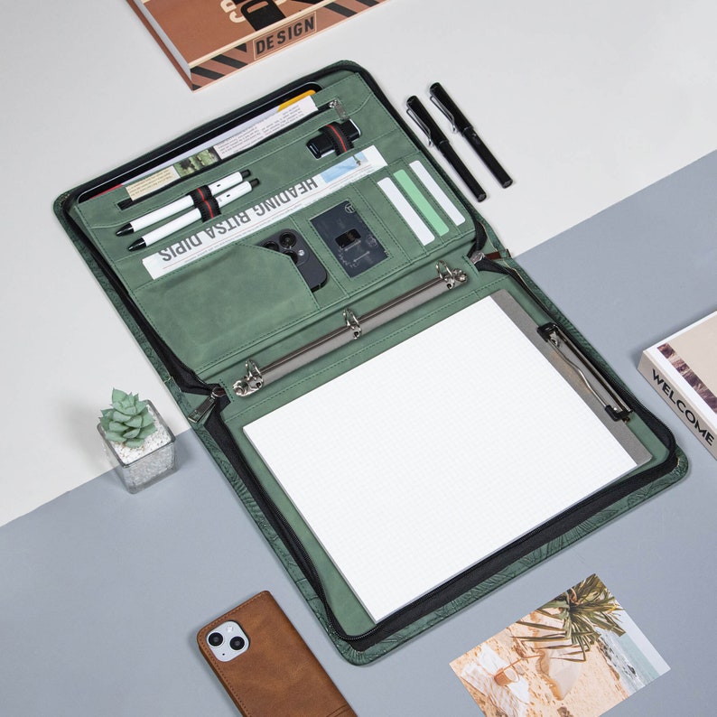 May include: A green leather binder with a zipper closure, a ring binder mechanism, and a built-in notepad. The binder has multiple pockets and slots for pens, cards, and other accessories. The text "Heading Bitsa Dips" is printed on the front of the binder.
