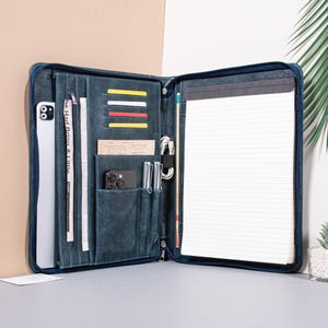 May include: Open, blue leather portfolio with multiple pockets and compartments. Includes a notepad, card slots, and a phone pocket. The portfolio is open, revealing a phone, cards, and a notepad. The portfolio is on a neutral background.