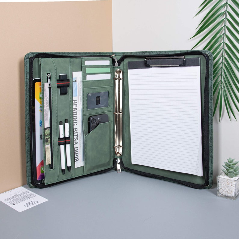 May include: A green leather zippered binder with a clipboard, pockets, and a ring binder. The binder is open and has a white lined notepad inside.