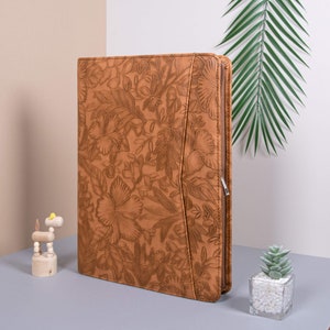 May include: A brown leather zippered binder with a floral pattern. The binder has a zipper closure and a silver zipper pull.