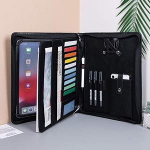 May include: Black leather portfolio with a zipper closure, multiple pockets, and a built-in iPad holder. The portfolio has a card holder, pen loops, and a phone pocket.