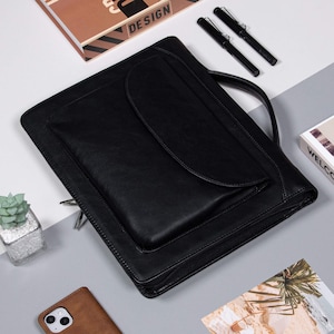 May include: Black leather portfolio with a zipper closure and a large pocket on the front. The portfolio has a handle on the top.