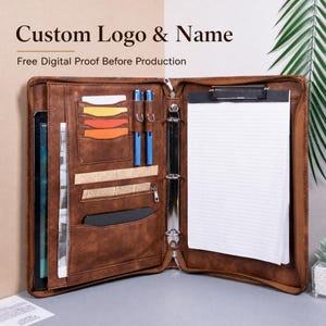 Peut inclure: Un porte-documents en cuir marron avec un classeur à trois anneaux, un presse-papier avec du papier ligné, plusieurs fentes pour cartes, deux stylos bleus et une pochette pour tablette. Le texte Custom Logo & Name et Free Digital Proof Before Production est visible.