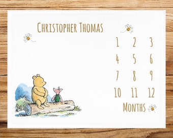 May include: A Winnie the Pooh and Piglet baby growth chart with a white background and gold text. The chart features a drawing of Winnie the Pooh and Piglet sitting on a log. The text "Christopher Thomas" is at the top of the chart. The numbers 1 through 12 are listed in columns, with the word "MONTHS" below the numbers.