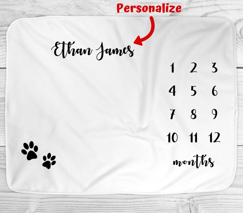 May include: White baby blanket with black paw prints and a personalized name, "Ethan James", and numbers 1-12 for monthly milestones.