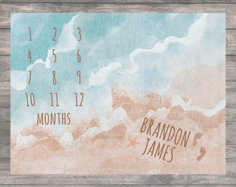 May include: A watercolour baby milestone growth chart with a beach theme. The chart features a blue and brown watercolour background with waves and sand. The numbers 1 through 12 are printed in brown along with the word "MONTHS". The name "BRANDON JAMES" is printed in brown at the bottom of the chart along with a starfish and two footprints.